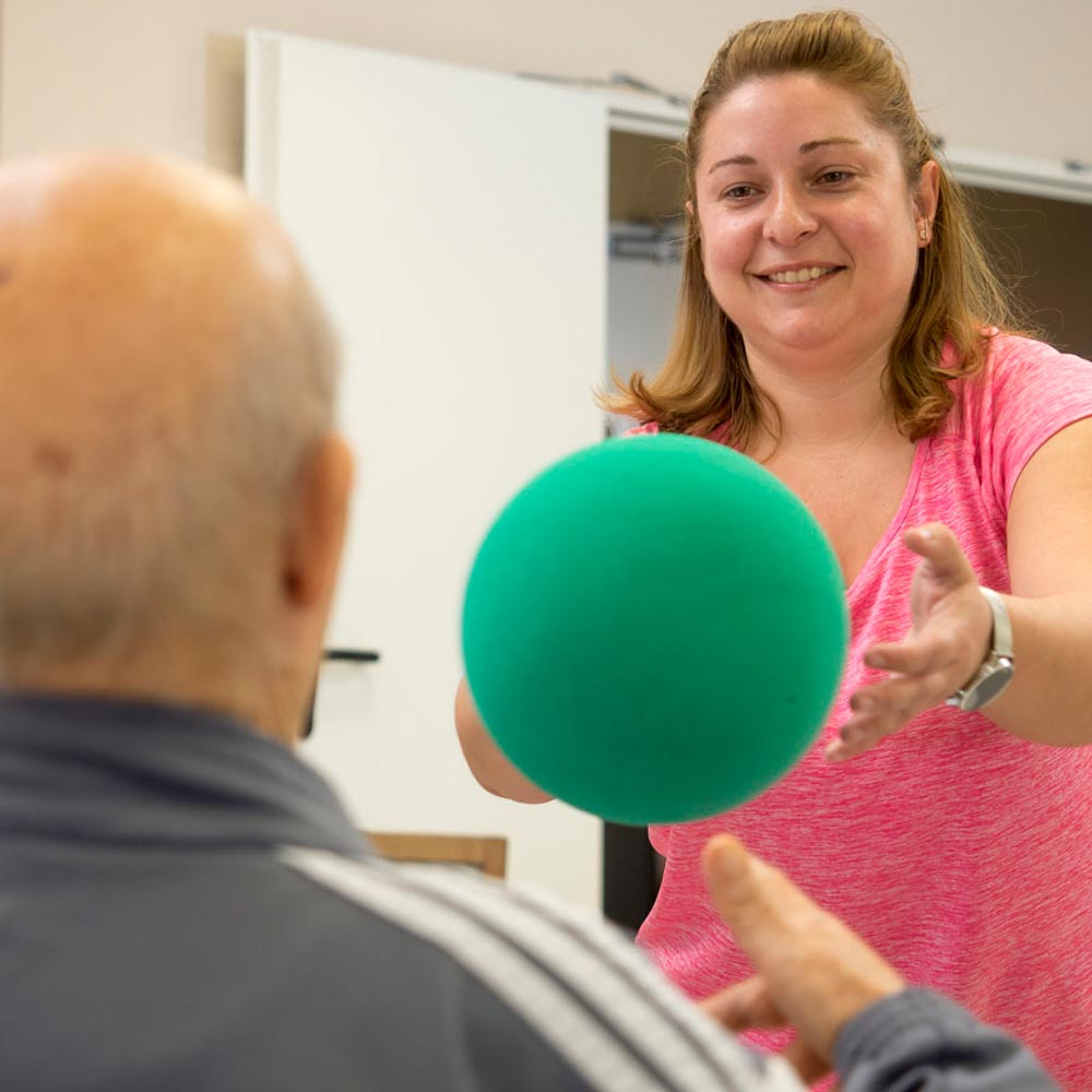 Una trabajadora del centro ayuda a un residente a realizar ejercicios de rehabilitación con una pelota